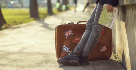 Your Costs and Benefits person leaning against a wall with a brown suitcase