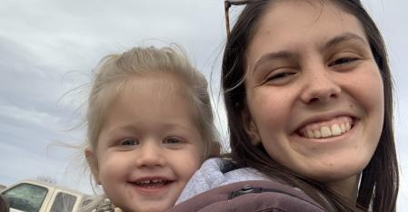 Duties of an Au pair au pair with a toddler girl in a back carrier smiling