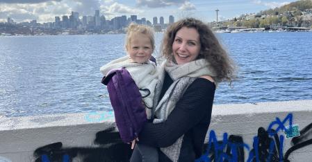 au pair holding her host daughter with the city skyline in the background