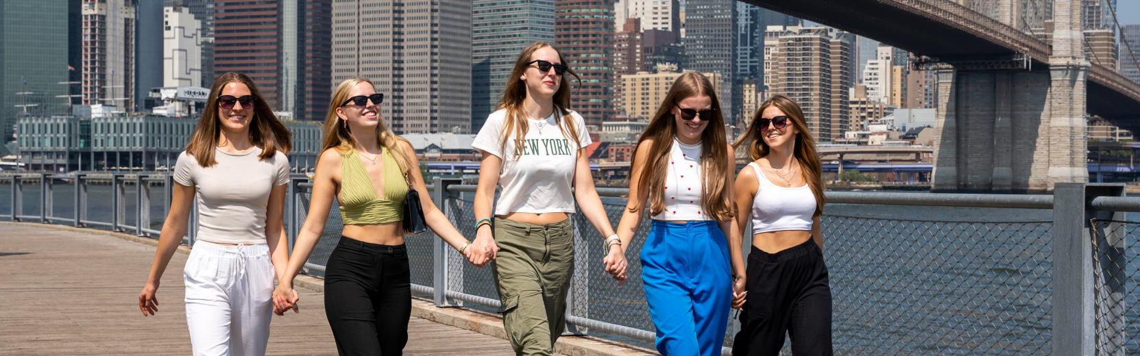 Discover the USA as an au pair group of smiling au pairs walking together by the Brooklyn Bridge.