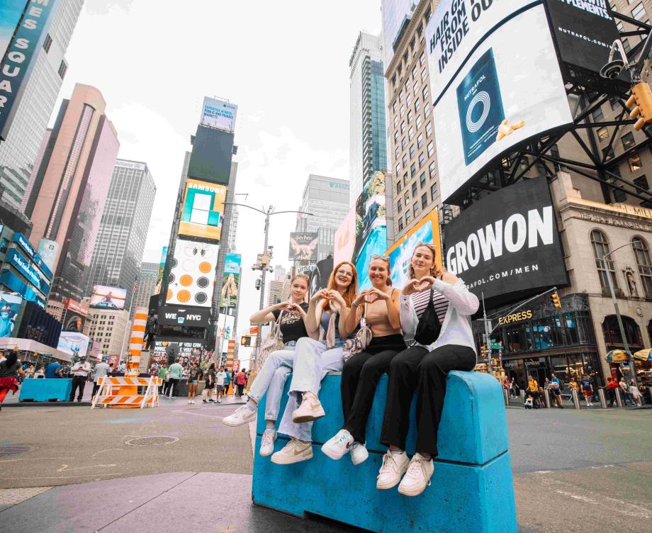group of au pairs sitting next to each other on a concrete block on Times Square